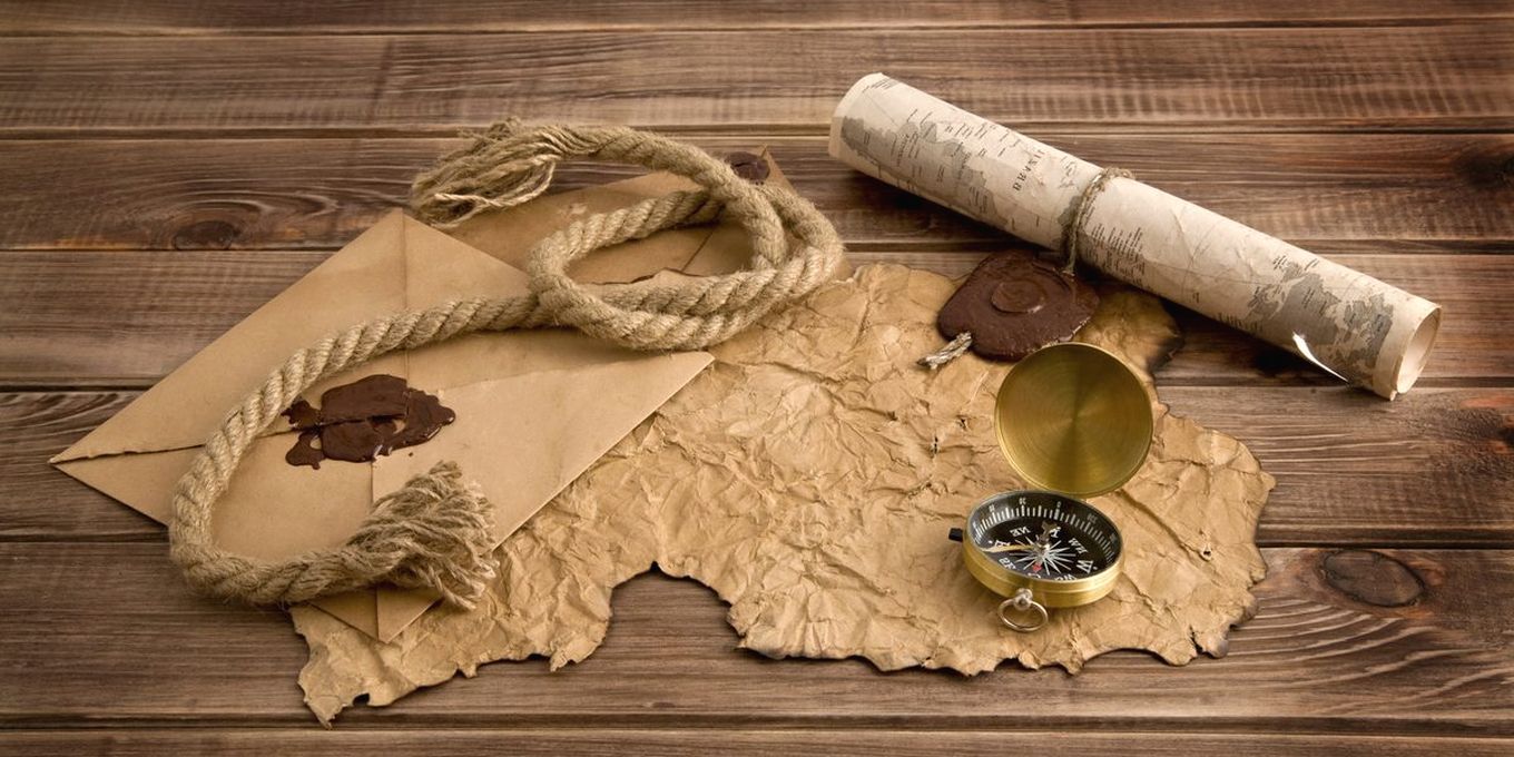 A paper map, a compass and a coil of rope on a wooden table