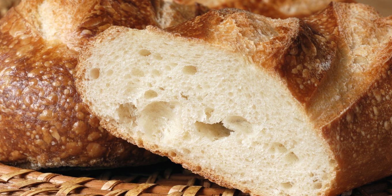 A broken loaf of crusty bread on a wicker tray